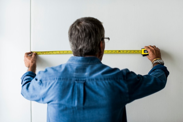 Homme prenant une mesure sur un mur avec un mètre ruban avant d'installer un paravent
